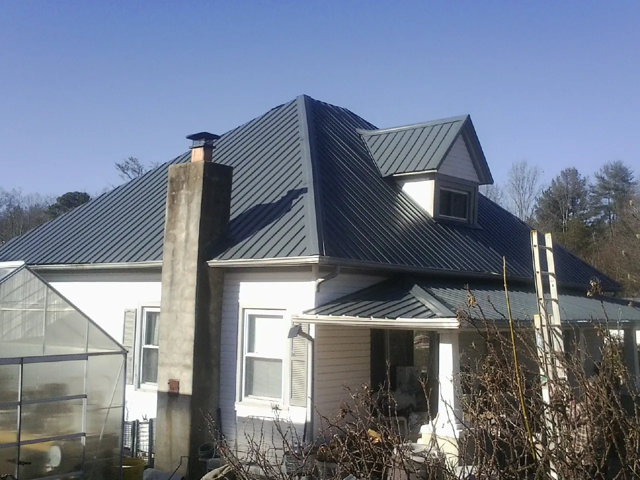 Dark blue standing seam metal roof on a white farmhouse with dormer — Slate & Tile Roof Repair by Roofing Brothers in Marquette