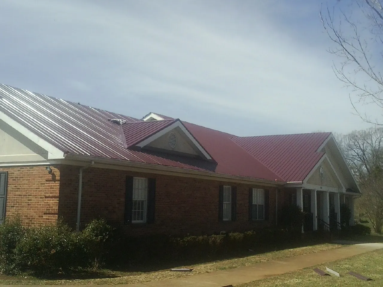 Red metal roof with gabled entries on a long brick building, from a Hail Damage Roof Repair job in Marquette