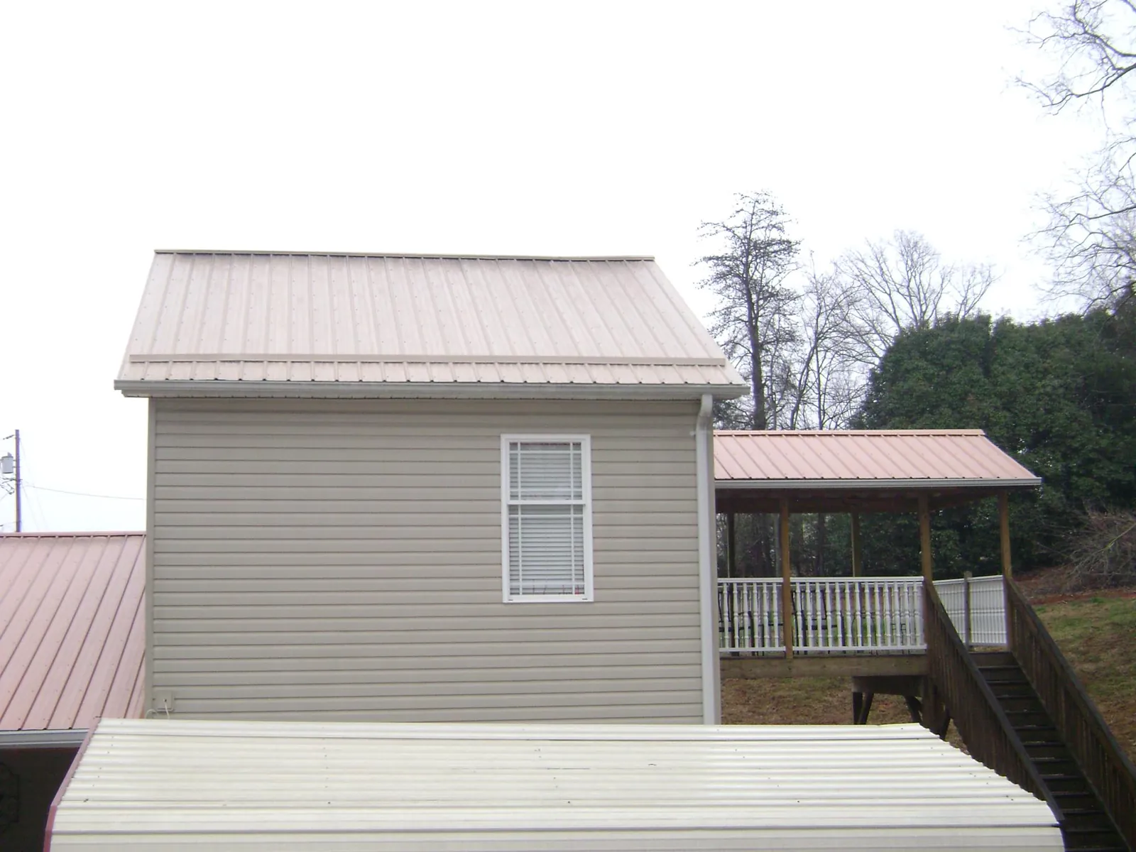 Tan metal roofs on a two story addition and attached porch, from a Roof Replacement job in Marquette
