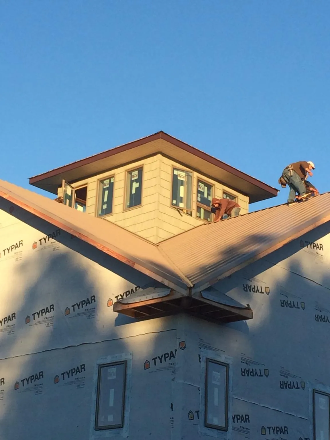 Roofers working around a rooftop cupola on a new metal roof at sunset — Roof Waterproofing in Marquette by Roofing Brothers